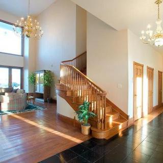 A spacious and modern foyer with a wooden staircase, illuminated by chandeliers.