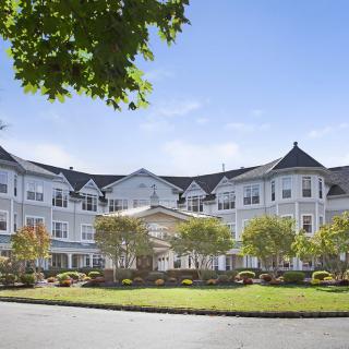 A large, elegant hotel building with a landscaped entrance and bright blue sky.