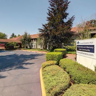 A paved driveway leads to a building with neatly trimmed shrubs and a sign at the entrance.