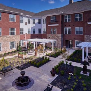 A peaceful courtyard with a fountain and seating area surrounded by a brick residential building.