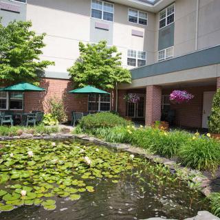 A serene garden with a pond and lilypads, adjacent to a building with outdoor seating.