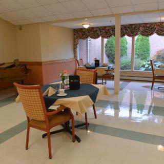 A cozy dining area with chairs and a table, illuminated by natural light from the windows.