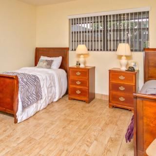 A cozy bedroom featuring two twin beds with wooden frames, two nightstands with lamps, and a window with blinds.