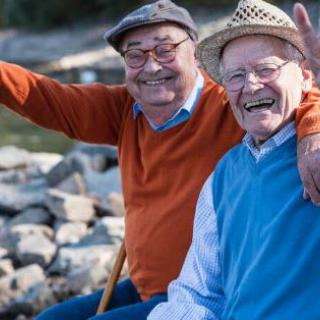 Two elderly friends smiling and enjoying time together outdoors by the water.