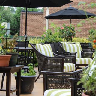 A cozy outdoor seating area featuring stylish wicker chairs with striped cushions, surrounded by greenery and shaded by black umbrellas.