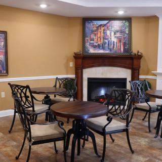 A cozy seating area with round tables, cushioned chairs, and a fireplace adorned with artwork.