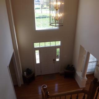A spacious foyer with a chandelier, large window, and hardwood floors.