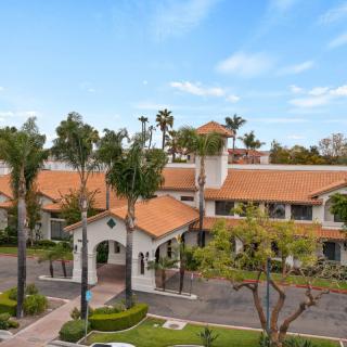 Aerial view of a building with orange-tiled roofs surrounded by palm trees.