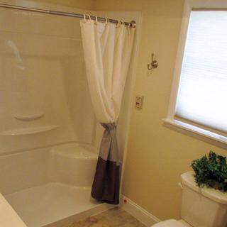 A bathroom with a shower, curtain, and toilet near a window.
