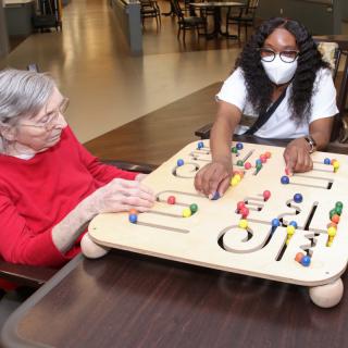 A caregiver and an elderly woman engage with an activity board in a nursing home setting.