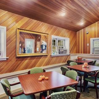 A cozy dining area featuring wooden paneling, tables with green upholstered chairs, and a large mirror on the wall.