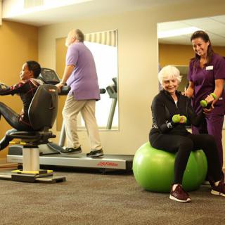 Seniors engaging in physical exercise at a gym, supported by a trainer.