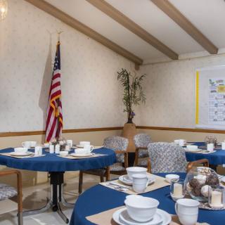 A dining area set up with tables featuring blue tablecloths, arranged with plates and cups, alongside an American flag displayed in the corner.