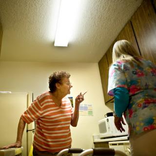 An elderly woman expresses her concerns while a caregiver listens attentively in a kitchen setting.
