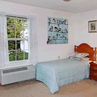 A cozy bedroom with a single bed, artwork on the wall, and a window overlooking greenery.