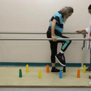 A person engages in physical therapy using support bars for balance, navigating colored cones on the floor.