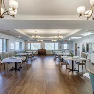An empty dining room with neatly arranged tables and chairs, featuring large windows and elegant chandeliers.