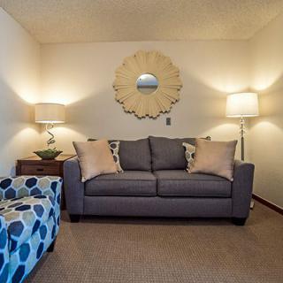 A cozy living room with a gray sofa, flanked by two standing lamps and accented with a decorative mirror on the wall.