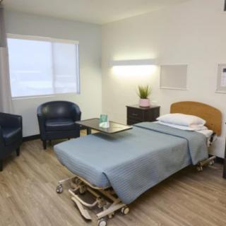A clean and minimalist hospital room featuring a bed, chairs, and a small table.