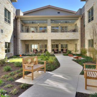 A courtyard with a garden pathway and benches surrounded by a multi-story building.
