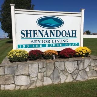 Outdoor sign for Shenandoah Senior Living on Lee Burke Road, adorned with colorful flowers.