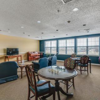 A cozy game room with tables and chairs, featuring a chessboard and a television.
