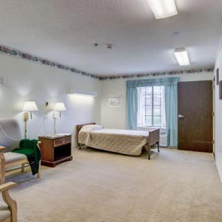 A minimalist bedroom with a single bed, chair, lamps, and a window.