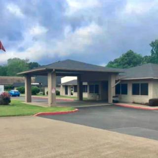 A building with a covered entrance, featuring a flag and landscaped surroundings under a cloudy sky.