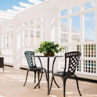 A sunlit patio with a table and two chairs under a pergola.
