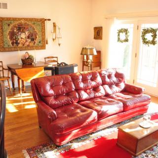 A cozy living room featuring a red leather sofa, bright natural lighting, and elegant decor.