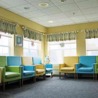 A colorful waiting room in a hospital with blue, green, and yellow chairs arranged around the space.