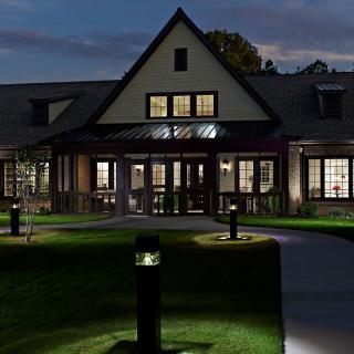 A well-lit building at night with a lawn and pathway leading to the entrance.
