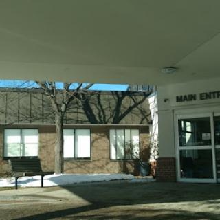 A view of the entrance to a building, featuring large windows and trees in the background.