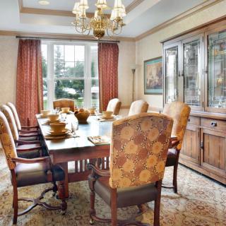 A well-decorated dining room featuring a large table with chairs, a chandelier overhead, and a cabinet against the wall.