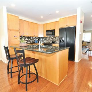 A modern kitchen featuring an island with bar stools, wooden cabinets, black appliances, and a granite countertop.