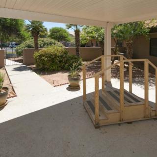 A covered patio area with a ramp leading to a garden with plants and a paved walkway.