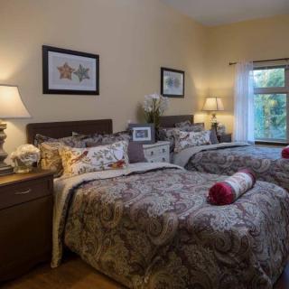 A cozy bedroom featuring twin beds with decorative bedding, illuminated by bedside lamps and adorned with framed artwork.