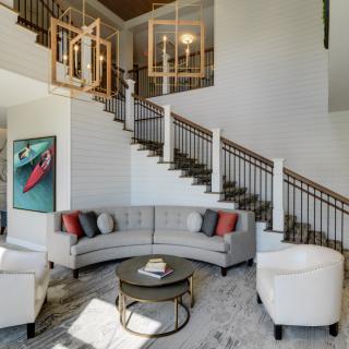 A modern living room featuring a large curved sofa, stylish artwork, and a prominent staircase with wooden railings.