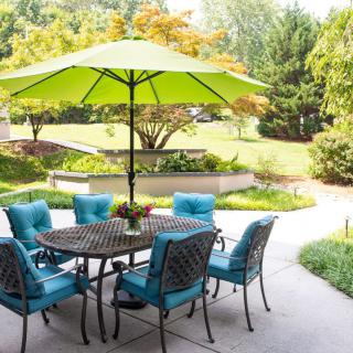 A cozy patio setup with a table, umbrella, and chairs in a lush backyard setting.
