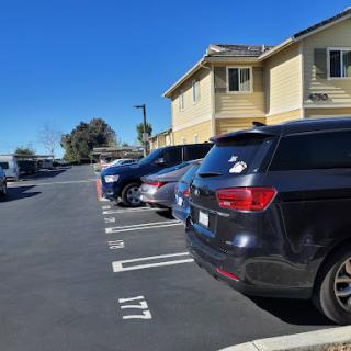 A view of a parking lot with several cars lined up beside residential buildings under a clear blue sky.