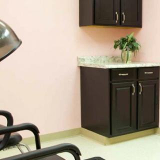 A modern hair salon with chairs, a hair dryer, and cabinets against a pink wall.