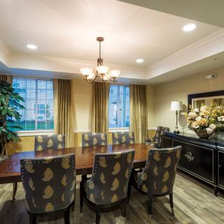 A well-lit dining room featuring a large wooden table with patterned chairs, illuminated by a chandelier, and adorned with elegant curtains and decor.