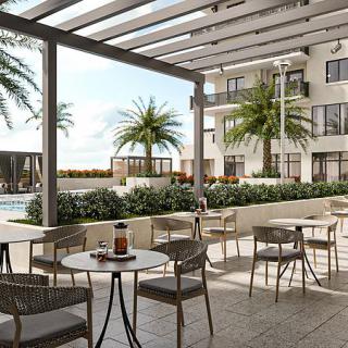 A modern outdoor patio with tables and chairs overlooking a pool area with palm trees.