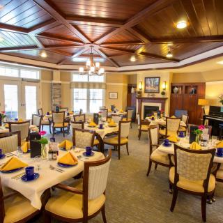 An elegantly decorated dining room with neatly arranged tables and chairs, featuring a wooden ceiling and chandeliers.