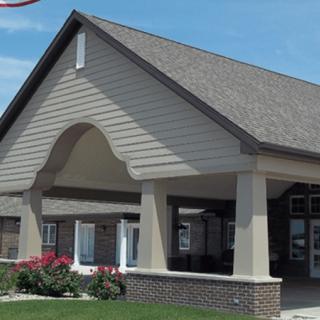 A building with a peaked roof and columns at the entrance, surrounded by landscaped greenery.