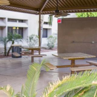 A covered outdoor patio area with benches and tables surrounded by plants.