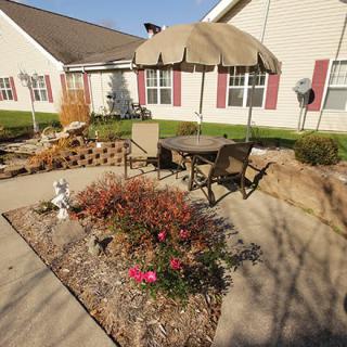 A sunny patio with outdoor furniture, an umbrella, and a small garden area.