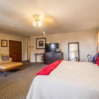A spacious bedroom featuring a large bed with red accents, a flat-screen TV, and cozy furnishings.