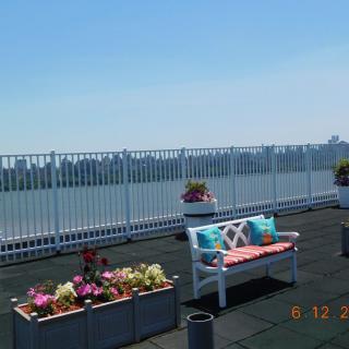 A rooftop garden with a bench and colorful flowers overlooking the city skyline.