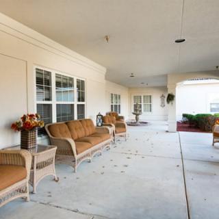 A covered porch with wicker furniture and decorative plants.
